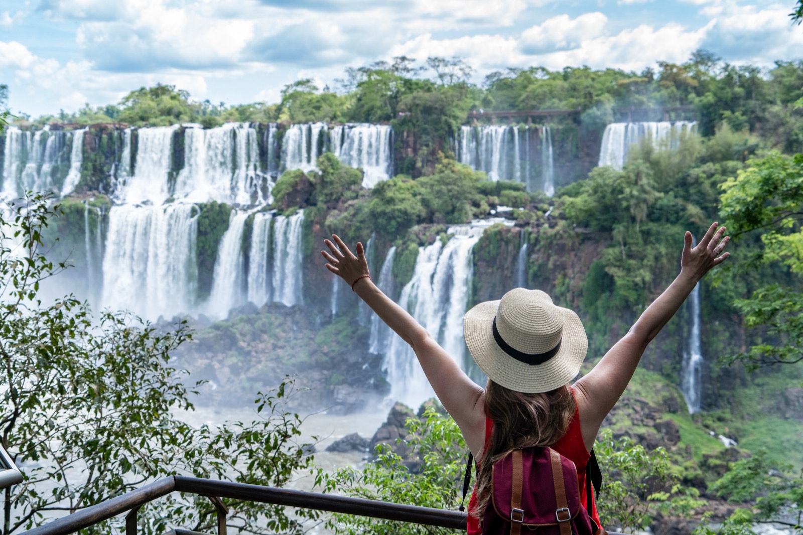 A traveller with arms raised in front of the Iguazú falls