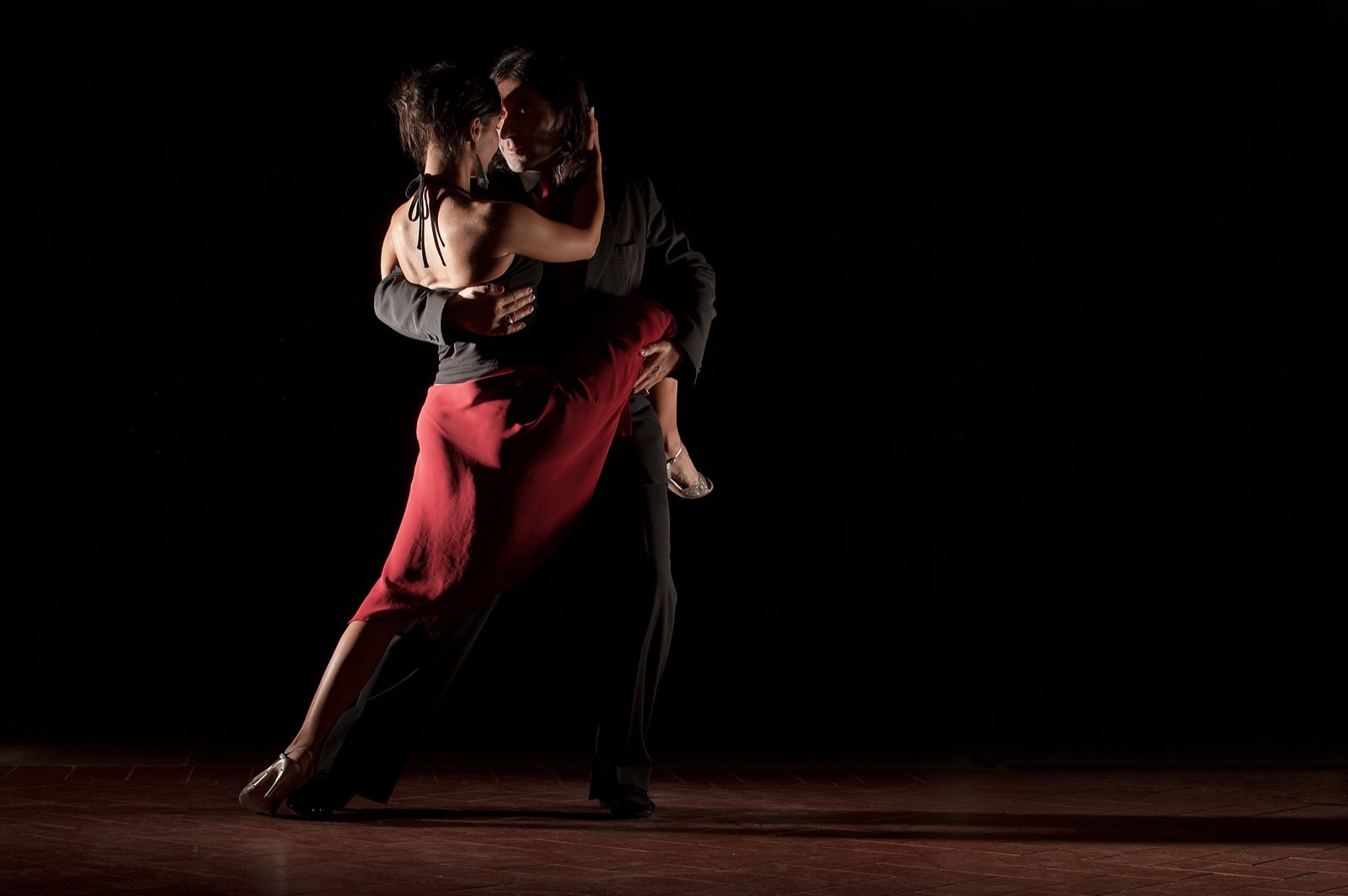 A tango couple in mid step under a stage light